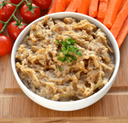 Bowl of tahini and onion dip with tomatoes and carrots in the background