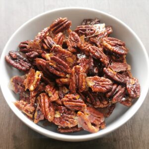 wooden surface with a white bowl of pecan brittle