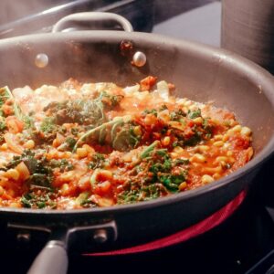 cast iron pan on a hob with beans pork tomato sauce and cabbage