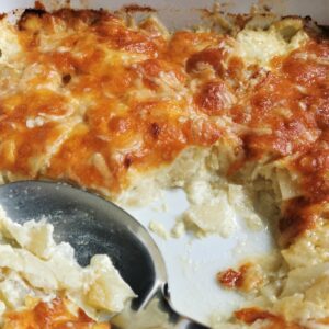 celeriac dauphinoise in a ceramic white dish and a spoon used to serve it