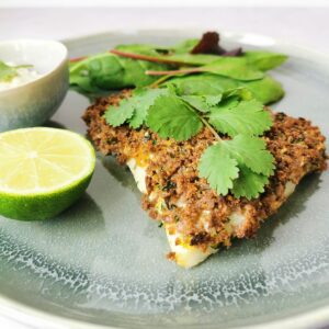 a piece of crumbed cod on a grey plate with half a lime, salad and a small bowl of tartare sauce