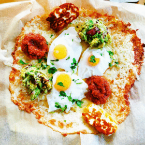 Low carb pizza base topped with 3 fried eggs, salsa, fried halloumi and guacamole with coriander sprinkled across it.