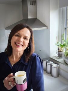 Natasha Hodge smiling holding a cup of coffee in her kitchen