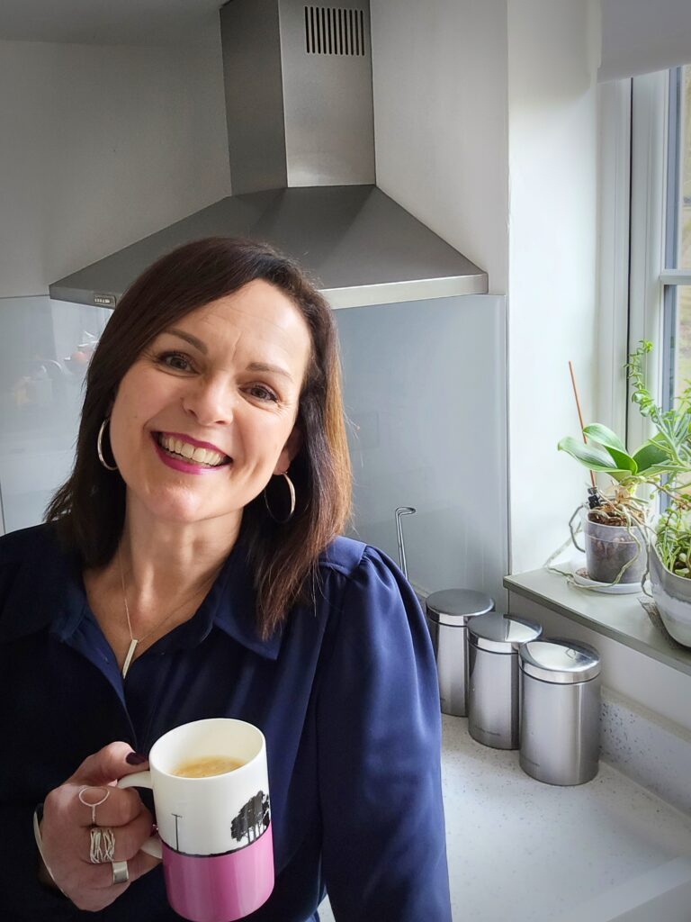 Natasha Hodge smiling holding a cup of coffee in her kitchen